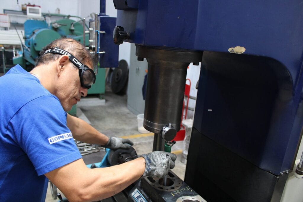 Técnico realizando el encamisado de cilindros en un compresor Copeland con máquina rectificadora de precisión
